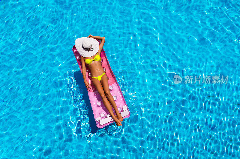 迷人的女人在比基尼放松在游泳池，俯视图