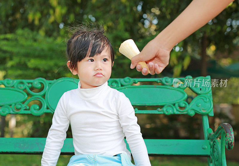 递给一个孩子冰淇淋，可爱的小女孩坐在公园的长椅上看着和无聊的糖果。