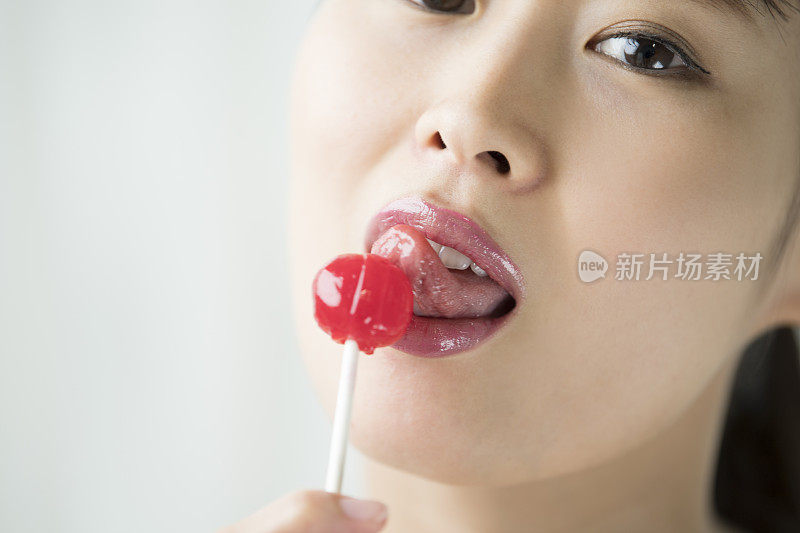 一个女人舔红色糖果的脸。