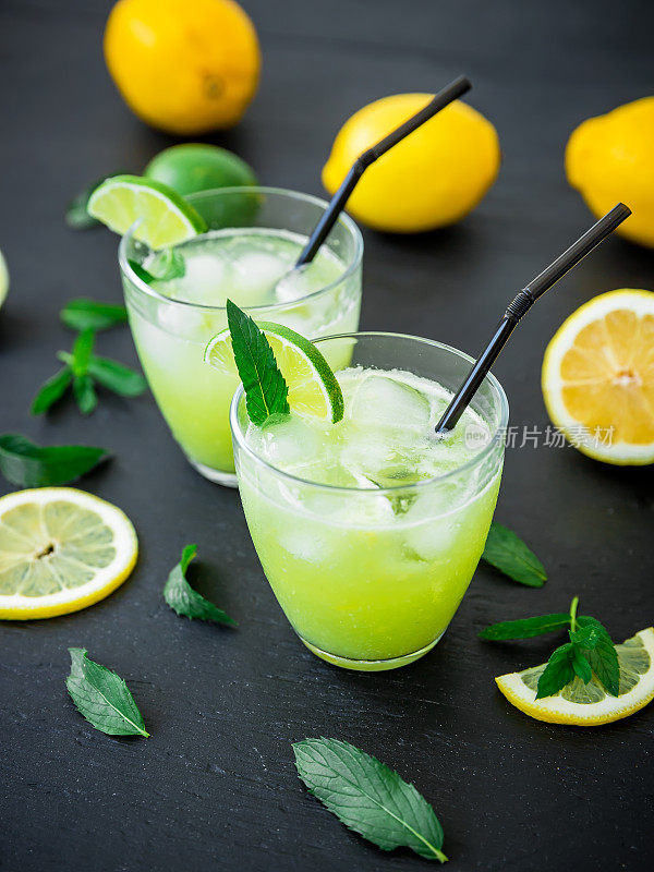 杯装酸橙和柠檬的清爽饮料。黑色的桌子上放着新鲜的柠檬水