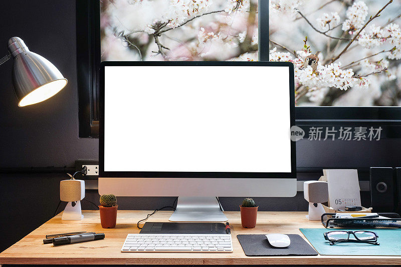 平面设计师的工作空间配备了一个手写板，一台电脑和白色的屏幕文本与美丽的樱花从窗口