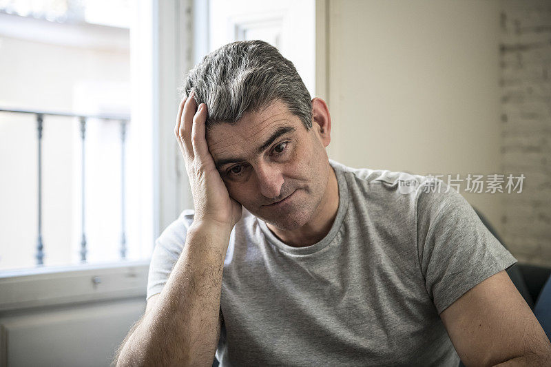 40岁或50岁悲伤和担心的人与灰色头发坐在家里的沙发上，看起来沮丧和浪费在悲伤的面部表情沮丧和生活问题的概念