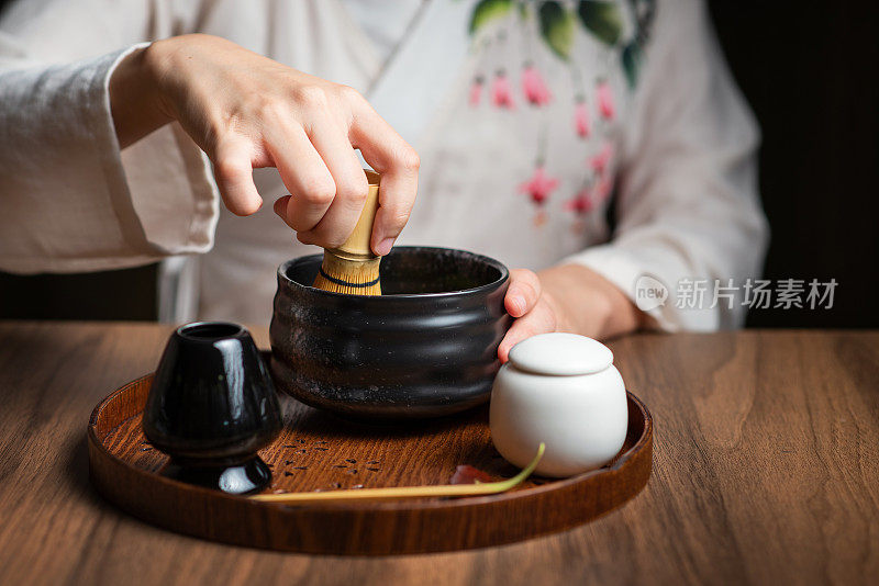 女士一边搅拌抹茶粉，一边用传统的茶道用具制作抹茶绿茶