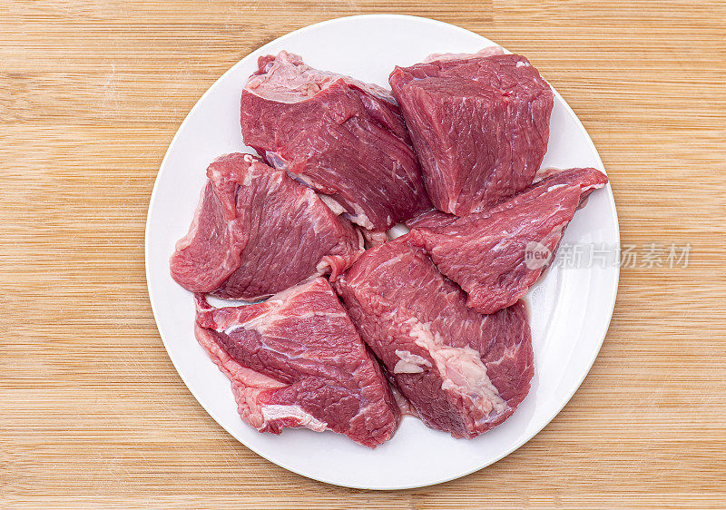 烧烤用的大块生牛肉或炖牛肉放在白色盘子上，俯视图