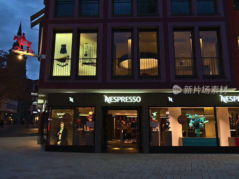 在市中心的市场上，Nespresso(咖啡胶囊)零售商店的正面视图，商店的窗户被灯光照亮，在晚上。