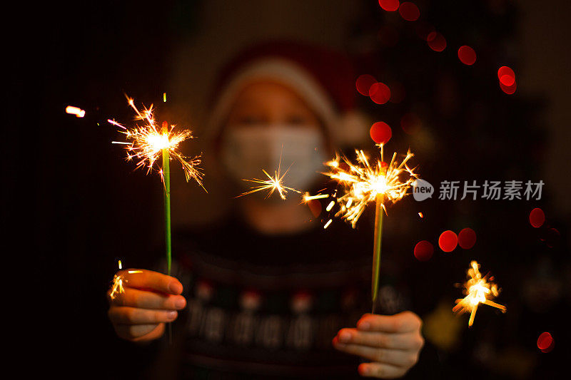 一个小男孩戴着医用面具和烟花在圣诞或新年派对上。