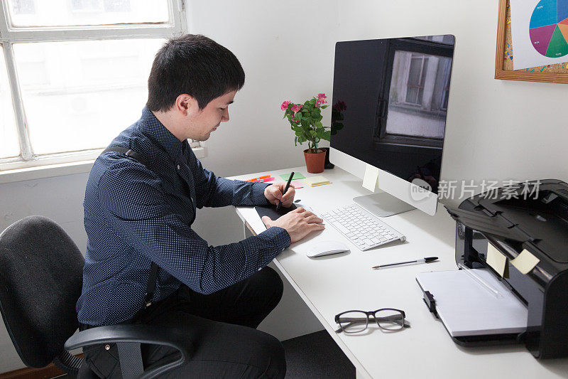 设计师在办公室的电脑前使用数字平板电脑工作。