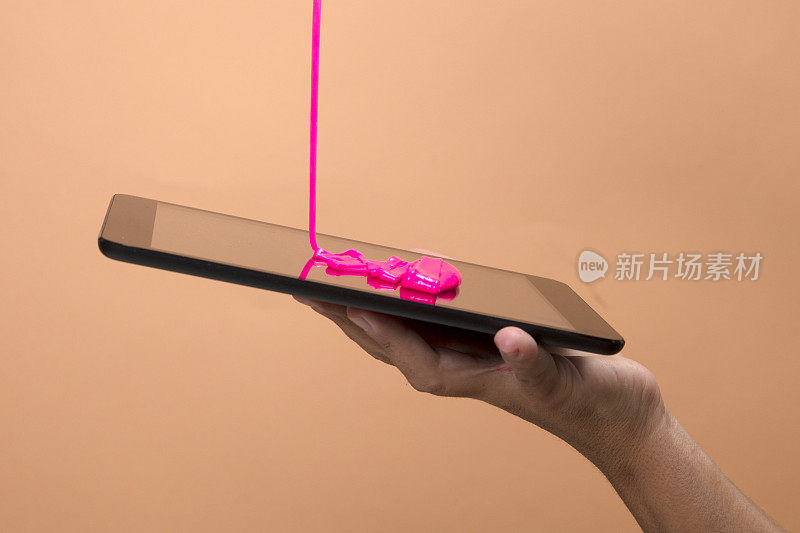 女人的手使用数字平板电脑与霓虹粉色黏液玩具在橙色波普艺术背景。