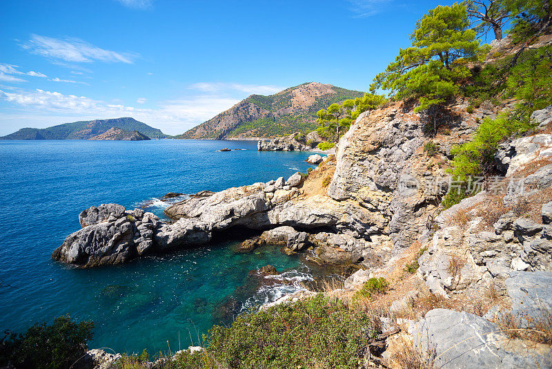 从山上眺望蔚蓝的地中海和松树，山坡上有岩石，天空湛蓝