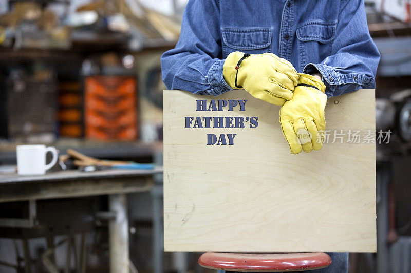 蓝领工人戴着工作手套举着“父亲节快乐”的牌子。