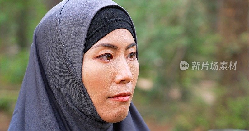 严肃沉思的中年亚洲穆斯林妇女看着远离肖像戴着头巾在一个公园摆姿势。