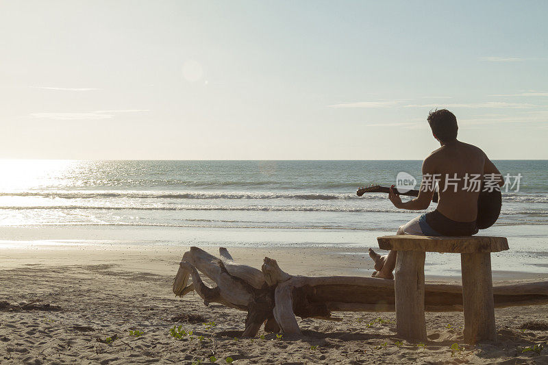 一个拉丁健康肌肉男子在海洋前弹奏原声吉他，放松在卡诺阿，Manabi省，厄瓜多尔，拉丁美洲