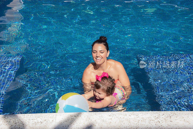 在一个阳光明媚的夏日，妈妈和小女儿在游泳池里玩耍