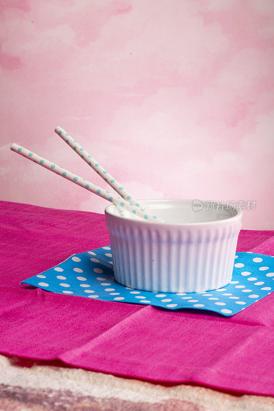 粉红色的瓷杯放在蓝色的餐巾和桌布上，里面是空的，还有两个蓝色的吸管