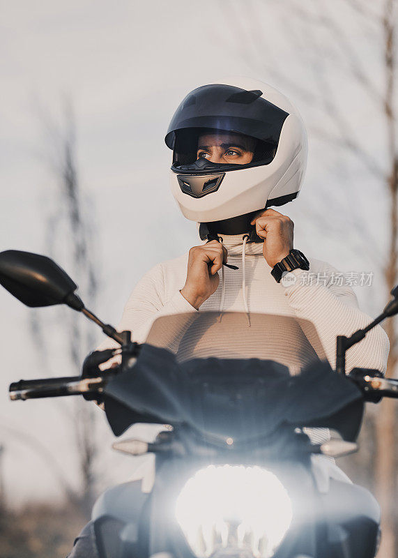 一个年轻人坐在摩托车上，把头盔戴在头上。