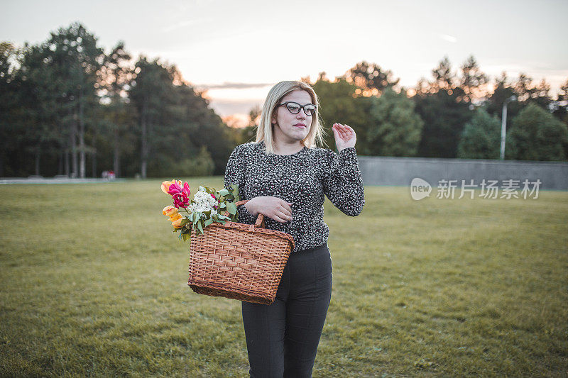兴高采烈的女人站在公园里，手里拿着野餐篮