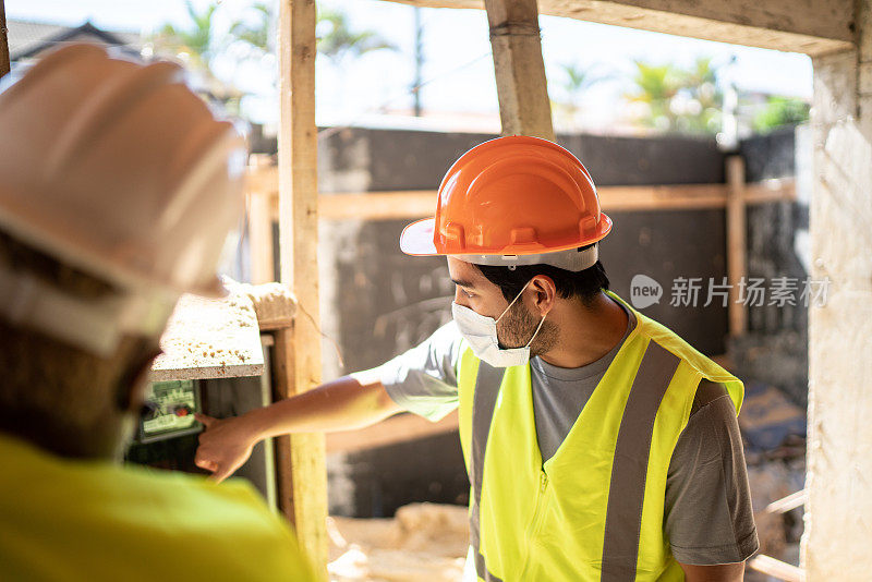 电工和建筑工人在工地开会，戴着防护口罩