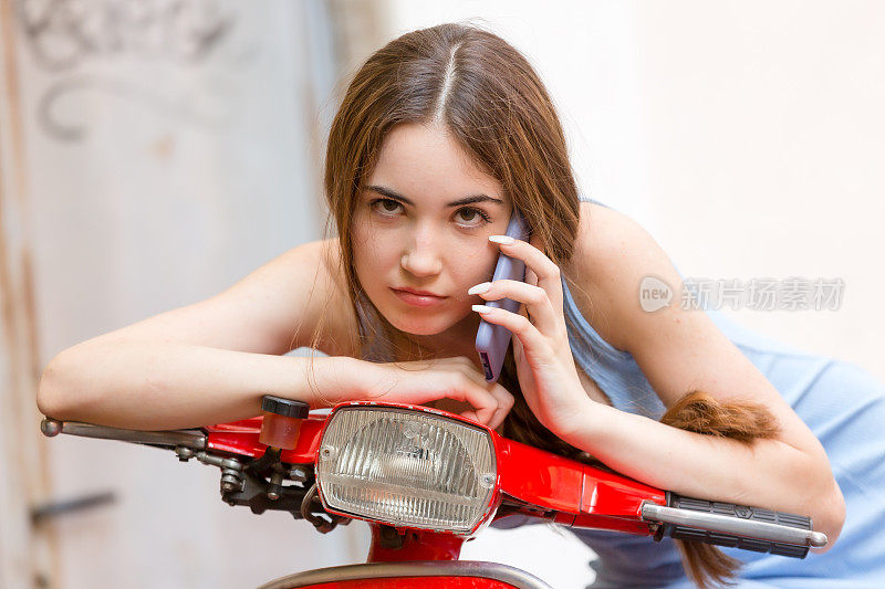 年轻女子坐在红色踏板车上打电话