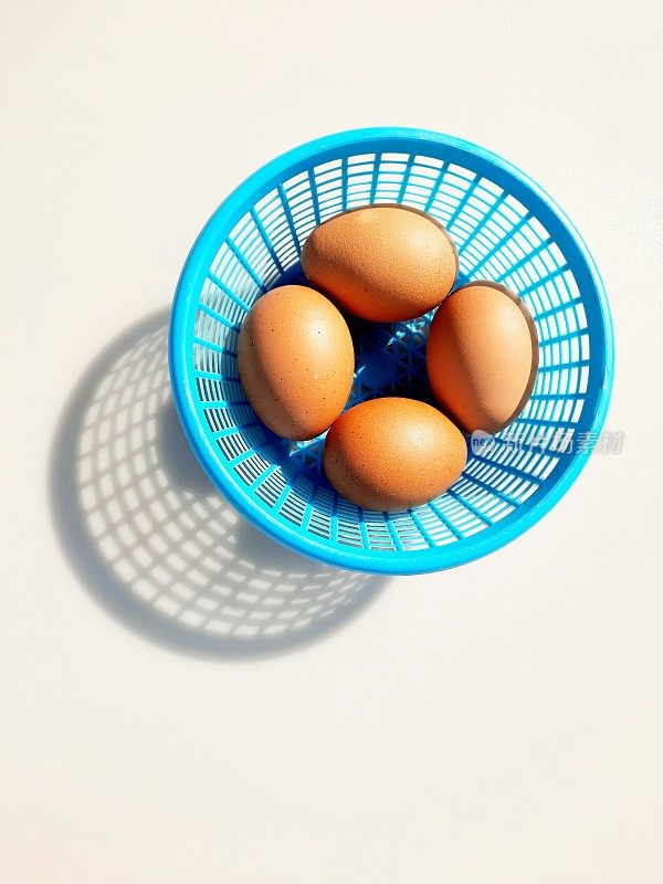 棕色鸡蛋在蓝色的篮子-白色的背景。