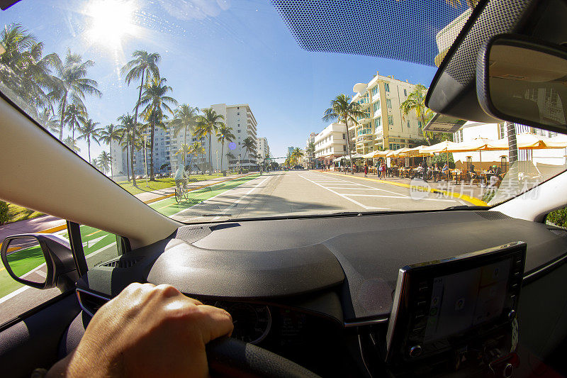 视角拍摄的一个年轻的运动男子驾驶汽车在迈阿密海滩地区的天堂蓝色的海洋景观，迈阿密，南佛罗里达，美国-美国