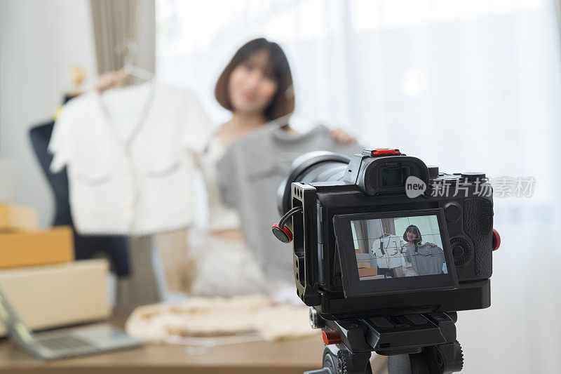 年轻美丽的亚洲女性博主在智能手机摄像头前展示衣服，同时录制vlog视频