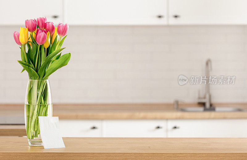 花束美丽的郁金香在厨房桌子上为您的消息与空白纸模糊厨房背景与地方蒙太奇产品显示