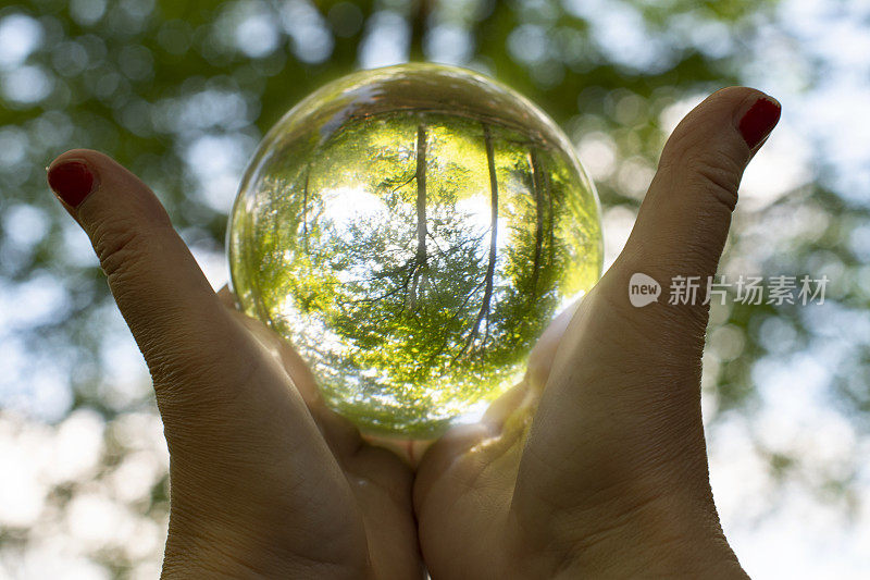 女性用红色指甲握着发光的水晶球，将自然包裹在里面，表现出女性对自然的关爱和气候