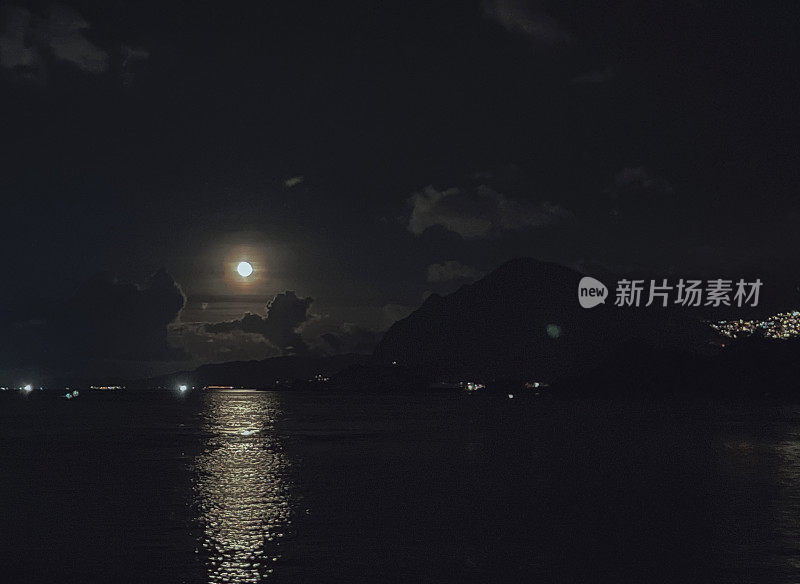 满月在夜晚升起在空旷的海面上，伴随着云和山峦