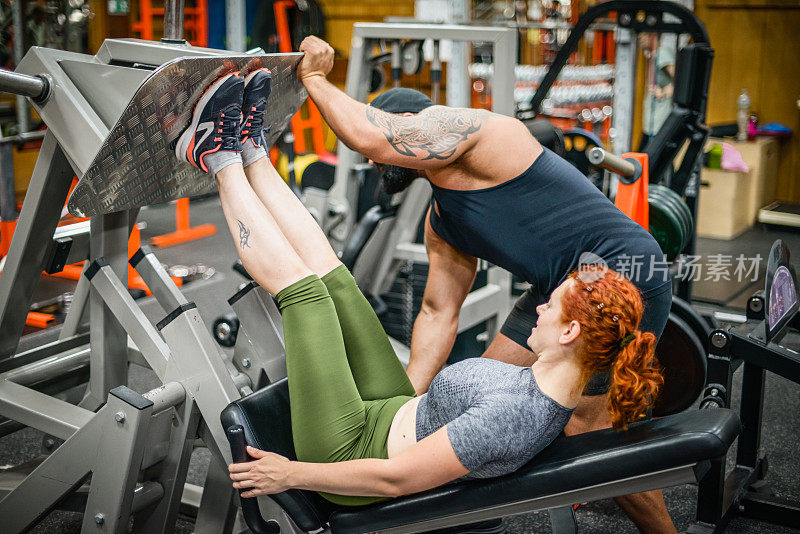 女人在健身房锻炼，一个男人教练运动体格