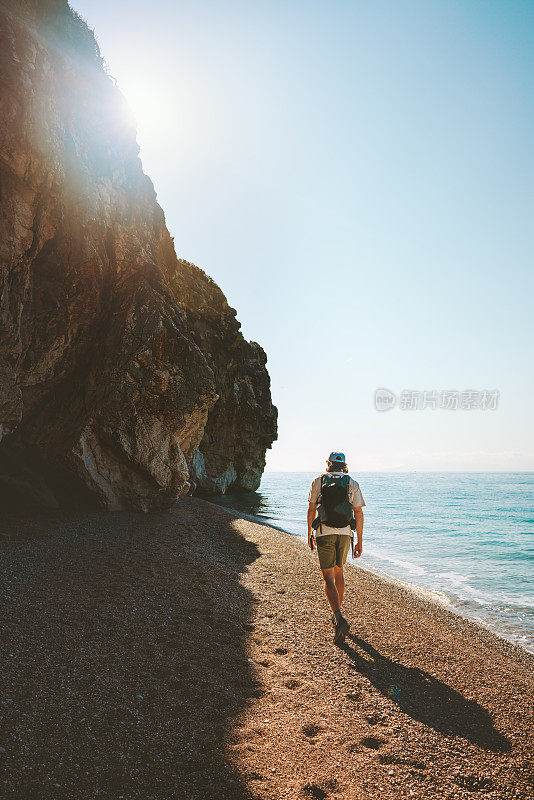 男子游客背着背包走在空旷的海滩上独自旅行，积极户外度假
