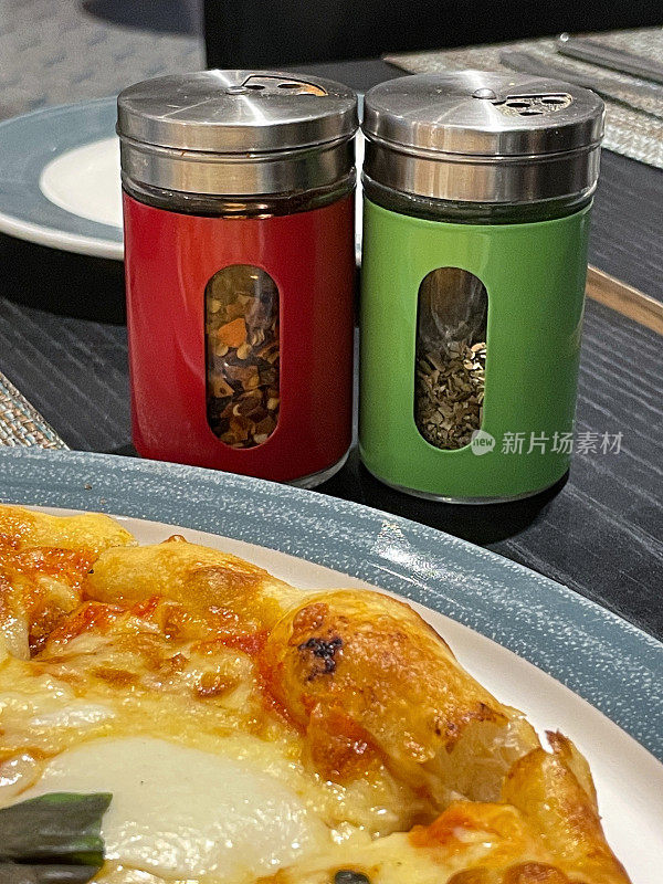 比萨餐厅餐桌的特写图像餐厅场景设置与摇瓶罐干香草和辣椒片，比萨玛格丽特在盘子上，瓶设置，重点在前景