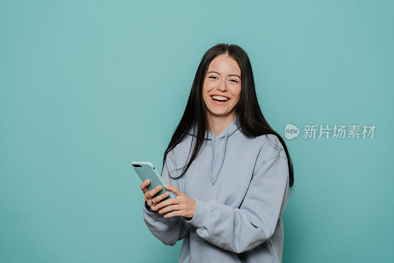 年轻美丽的白人女子使视频电话在蓝绿色的背景与一个快乐的脸站着，微笑着自信的微笑露出牙齿。人的沟通理念。