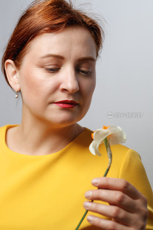 中年妇女的肖像，穿着黄色上衣，拿着水仙花，深情地看着它