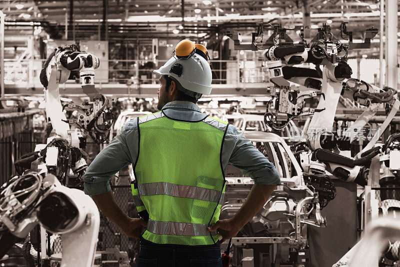 智能工厂机器人自动焊接工作控制机上，机械工程师头戴安全帽，身穿制服后视图