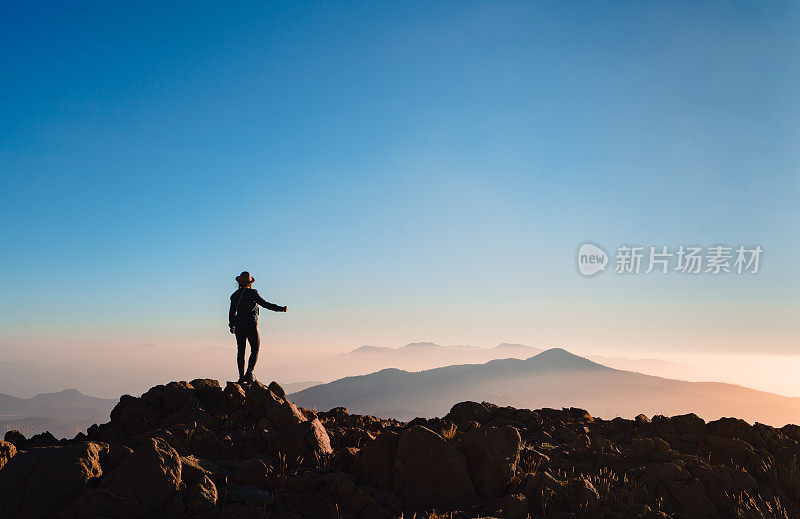 一个登山妇女的剪影在山顶上看日出