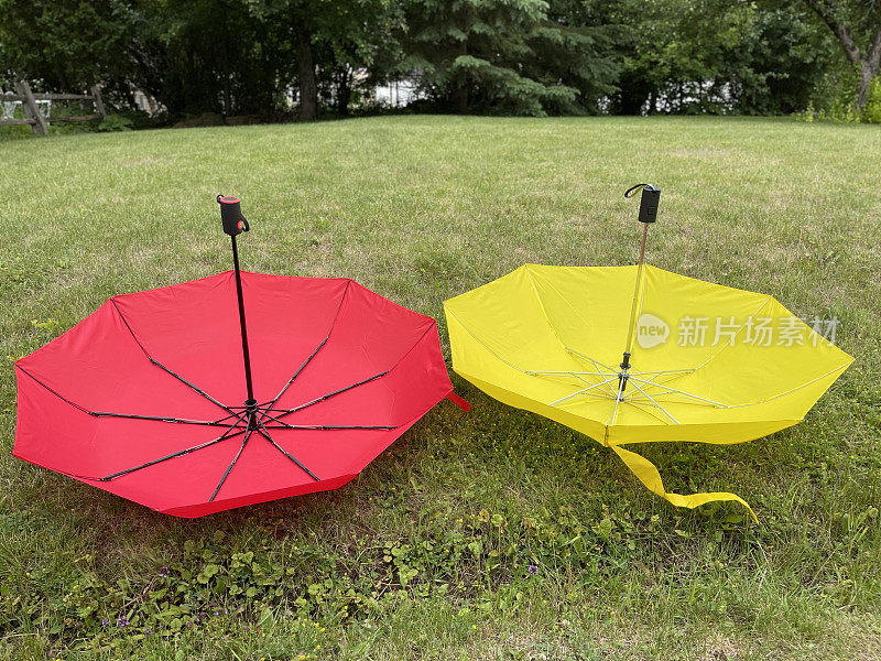 红色和黄色的伞开着，倒在草地上
