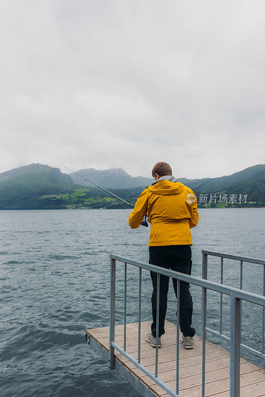 身穿黄夹克的男子在挪威峡湾边钓鱼