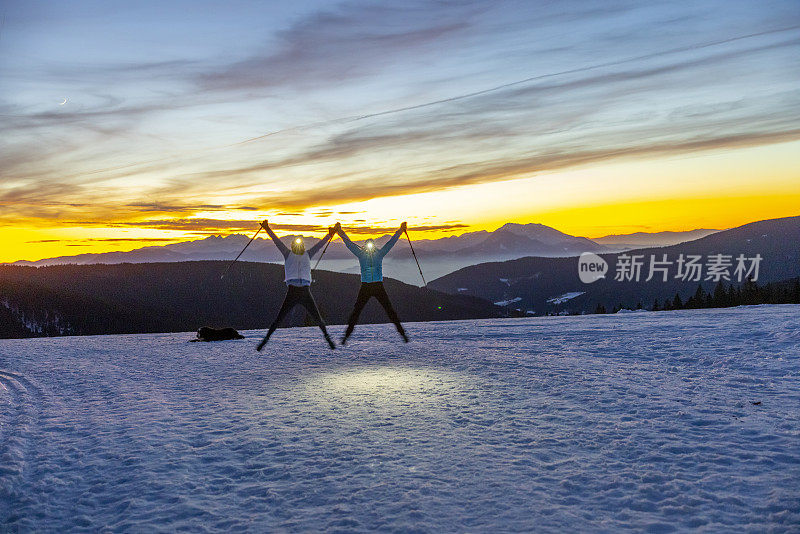滑雪假期，两个女人拿着滑雪杖在雪地上跳跃