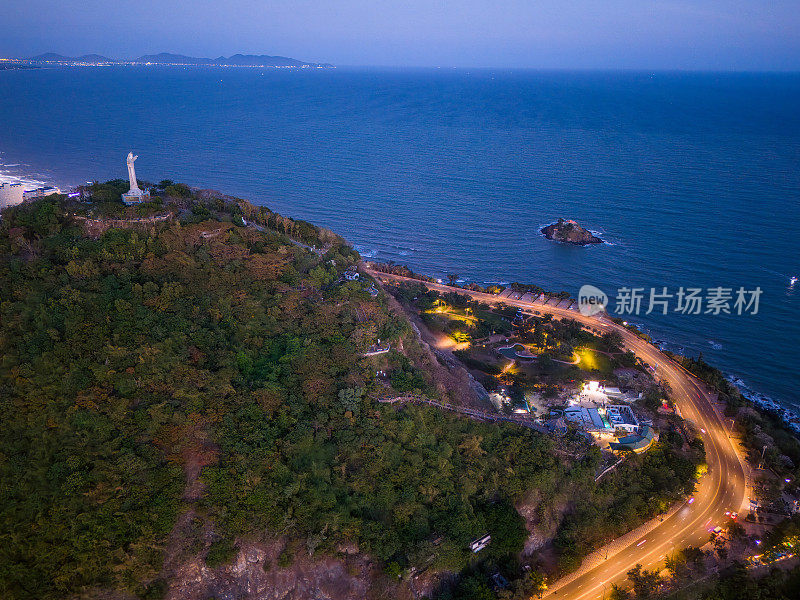 从上面俯瞰云头海岸全景，海浪、海岸线、街道、椰子树、越南Nho山后面的基督国王雕像