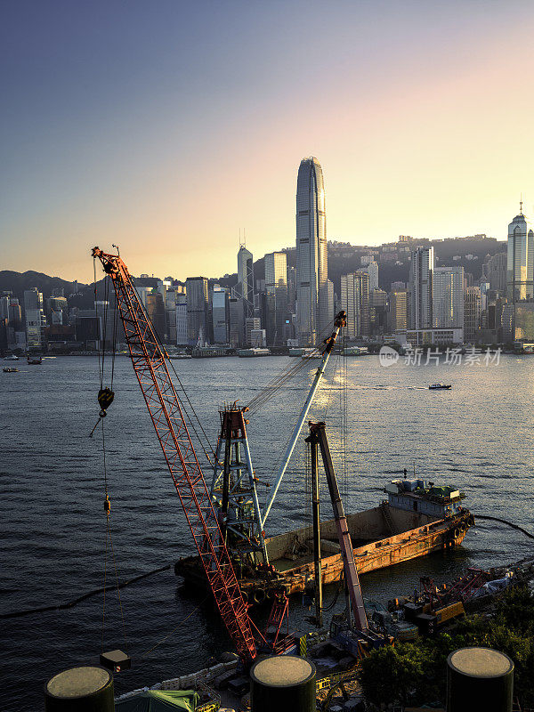 在以香港岛中心为背景的西九龙文娱艺术区海滨，打桩机、吊车和船吊正在工作。