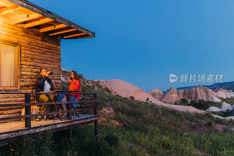 带着狗的男人和女人在露台上放松，欣赏乡村风景的黄昏