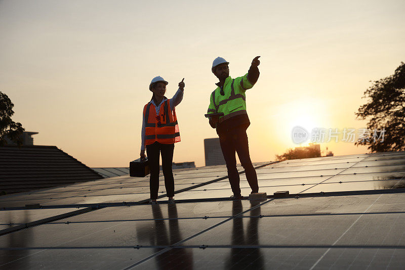 工地上的男女太阳能工程师们拿着工具箱在屋顶上顶着夕阳工作