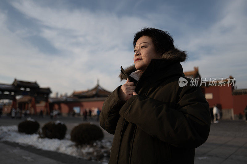 站在中国古建筑前，亚洲女游客微笑着望向别处