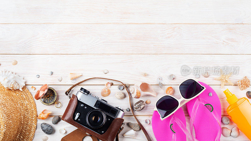 度假旅行策划背景，白色木板上的胶片相机、指南针、草帽、人字拖、太阳镜等沙滩属性的复制空间