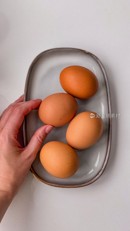 白色的桌子上，灰色的盘子里放着煮熟的棕色鸡蛋。传统的复活节概念。