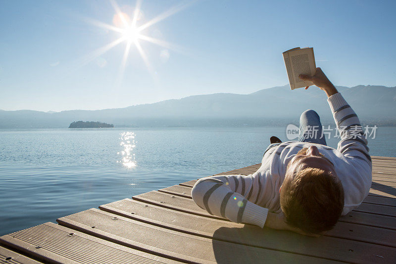 年轻人在湖边码头上放松，看书