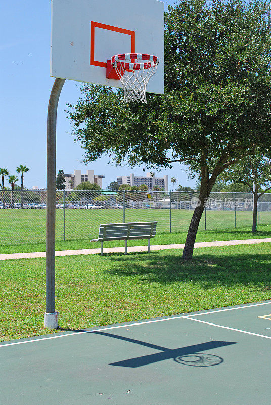 空篮球场加上篮筐和公园长椅和树