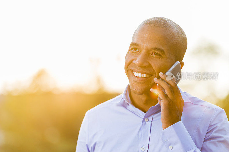 日落时分，微笑的非裔美国商人在用智能手机交谈。