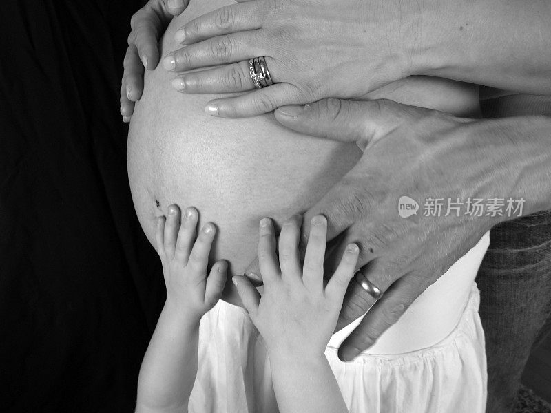 家人的手放在一个怀孕的肚子上