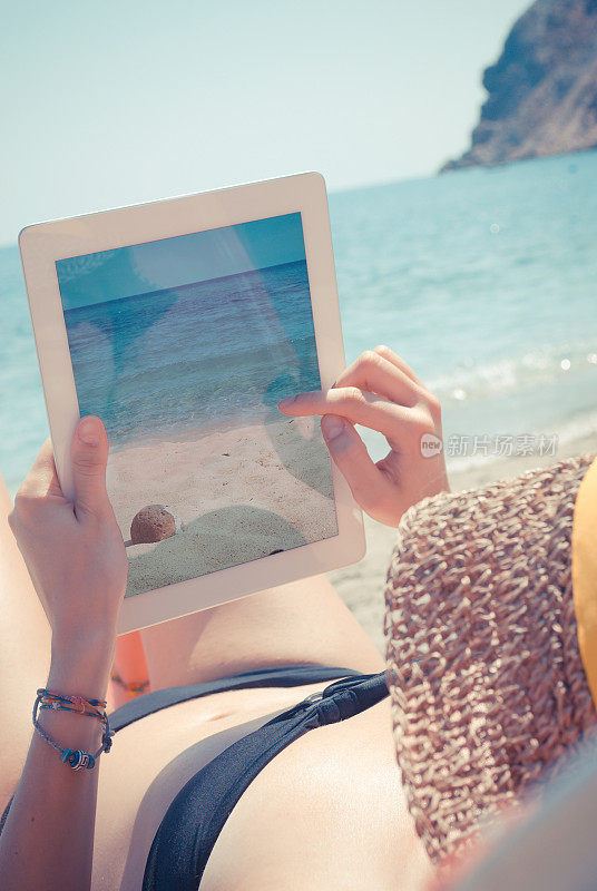 一个女人正在用平板电脑在海滩上拍照